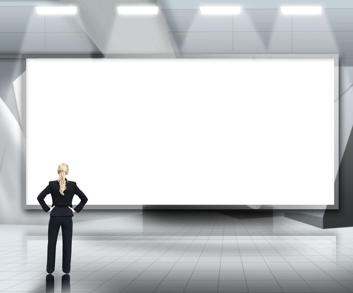 Businesswoman looking up at large blank screen under lights on grey background